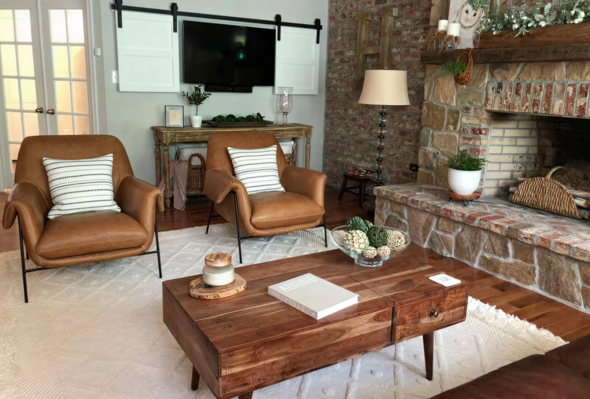 Two tan leather armchairs facing a wood coffee table beside a stone fireplace